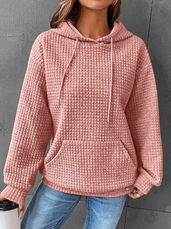 Vrouw in roze geruite hoodie met capuchon en kangoeroezak, casual outfit, grijze achtergrond, trendy damesmode, comfortabele kledingstijl.