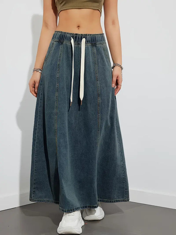 Vrouw in lange denim rok met elastische tailleband en witte trekkoorden, gecombineerd met witte sneakers. Trendy casual damesmode.
