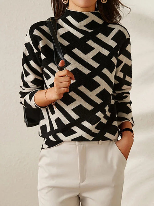 Dame in zwart-witte geometrische trui met hoge hals, draagt een zwarte tas en witte broek. Modieuze herfstkleding, trendy damesmode.