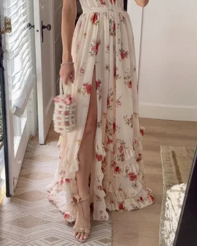 Vrouw in elegante, lange bloemenjurk met hoge split, houdt een stijlvolle handtas vast. Perfect voor zomerse evenementen en bruiloften.