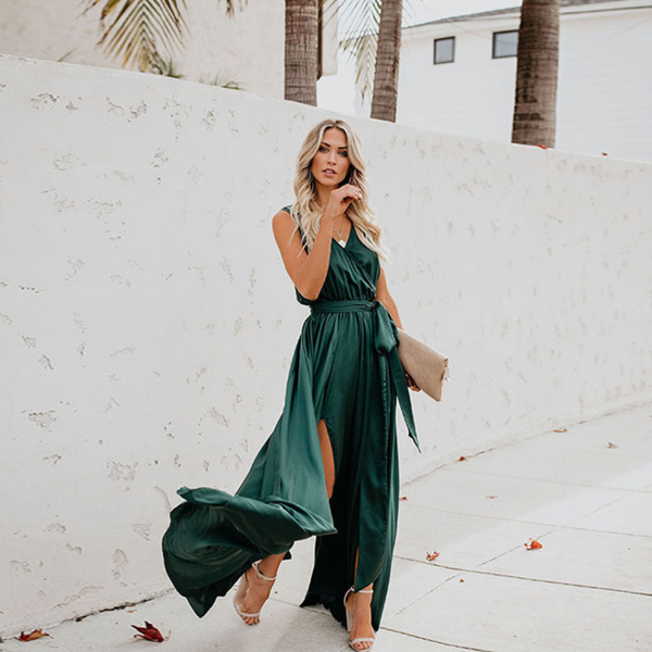 Vrouw in elegante groene maxi-jurk met hoge split, wandelend op trottoir. Zomermode, stijlvolle avondjurk, trendy dameskleding.