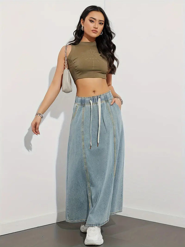 Vrouw in trendy outfit met olijfgroene crop top, lange denim rok en witte sneakers, poseert tegen witte achtergrond. Mode, casual, streetwear.