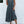 Vrouw in elegante, mouwloze, grijze zomerjurk met knopen, staand tegen witte muur. Perfecte outfit voor casual zomermode.
