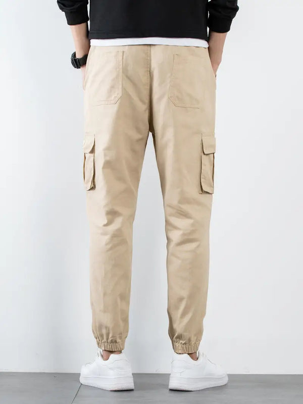 Beige cargobroek voor heren, achteraanzicht, met elastische enkels en zakken, casual streetwear, gecombineerd met witte sneakers.