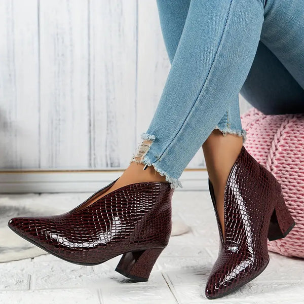 Donkerrode, glanzende enkellaarsjes met krokodillenprint en blokhak, gedragen met lichtblauwe, gerafelde skinny jeans. Stijlvolle damesmode.