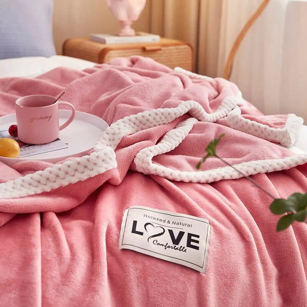 Roze fleece deken met witte rand op bed, naast roze mok en dienblad met fruit. Label met tekst "Relaxed & Natural Love Comfortable". Gezellig slaapkamerdecor.