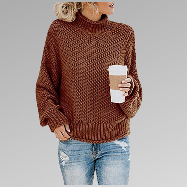 Vrouw in bruine gebreide trui met col, houdt een kartonnen koffiebeker vast, draagt gescheurde blauwe jeans. Casual herfstmode.