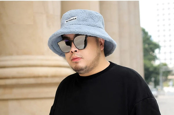 Man met grijze bucket hat en zonnebril, draagt een zwart T-shirt. Stijlvolle modeaccessoires, stedelijke achtergrond, casual look.
