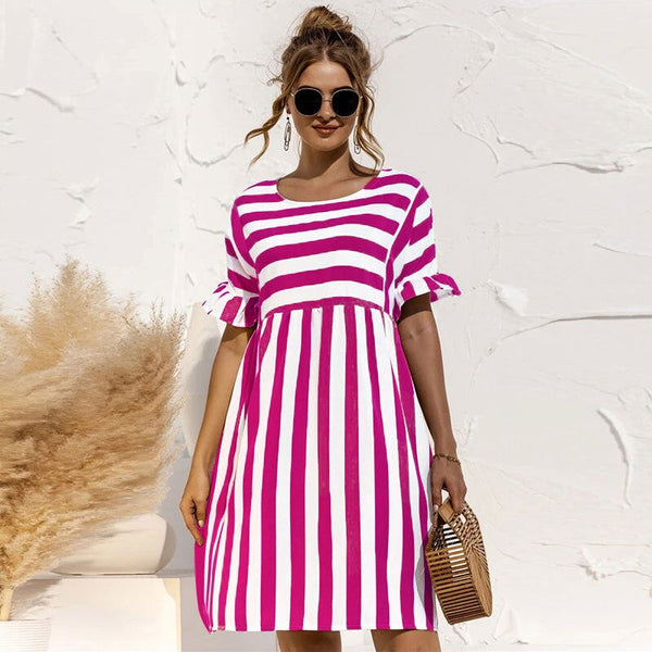 Vrouw in roze-wit gestreepte jurk met zonnebril, rieten tas, staand voor witte muur. Zomerjurk, casual mode, dameskleding.