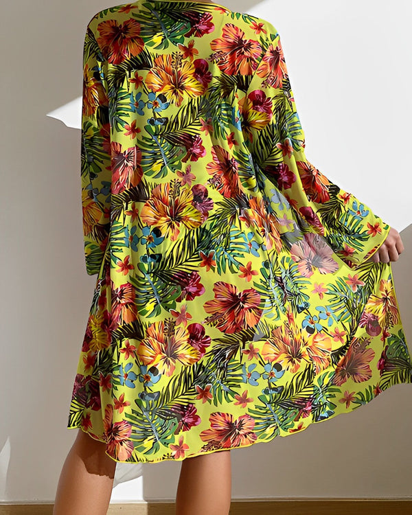 Vrouw in kleurrijke bloemenjurk met tropisch patroon, geel en rood, in zonlicht. Zomermode, casual strandkleding, trendy damesjurk.
