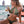 Vrouw in groene bikini met gevlochten haar drinkt cocktail op strand, zittend op oranje handdoek. Zomermode, strandvakantie, tropische sfeer.