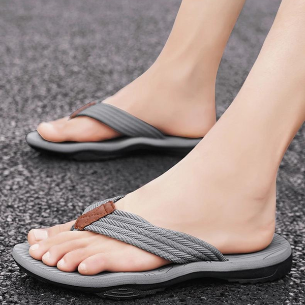 Grijze teenslippers met gevlochten band op asfalt, comfortabele zomerschoenen voor heren, ideaal voor casual strand- en stadswandelingen.