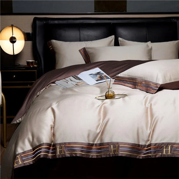 Luxe satijnen dekbedovertrek met bruine en gouden accenten, gestileerd met een modern nachtkastje en lamp. Perfect voor een elegante slaapkamerinrichting.