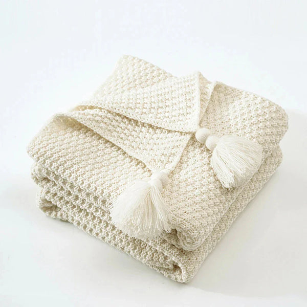 Gevouwen crèmekleurige gebreide deken met kwastjes, zachte textuur, perfect voor interieurdecoratie en comfort. Ideaal voor woonkamer of slaapkamer.