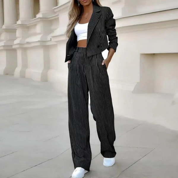 Vrouw in zwart-wit gestreept pak met crop top en sneakers, poseert voor klassieke architectuur. Modieuze dameskleding, zakelijke casual stijl.