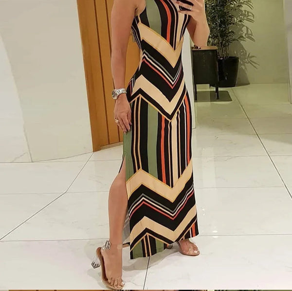 Vrouw in lange jurk met kleurrijke zigzagstrepen, staand op witte tegelvloer. Trendy zomerjurk, mouwloos, met split. Perfect voor casual en chique gelegenheden.