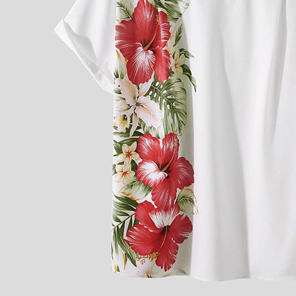 Witte blouse met kleurrijke bloemenprint, waaronder rode hibiscusbloemen en groene bladeren. Perfect voor zomermode en casual outfits.