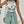 Vrouw in zomerse outfit met bloemen haltertop en mintgroene shorts, rieten schoudertas, strandkleding, casual mode, trendy dameskleding.