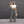 Vrouw in grijze flared broek en witte crop top voor grijze muur, draagt zonnebril en houdt beige tas. Modieuze dameskleding, casual stijl.