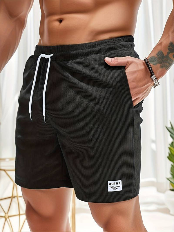 Man in zwarte sportshorts met witte trekkoord, hand in zak. Comfortabele herenkleding, casual zomeroutfit, fitnessmode.