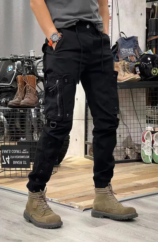 Man in zwarte cargobroek en bruine laarzen, staand in een winkel met motoraccessoires. Casual mode, herenkleding, outdoor stijl.