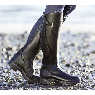 Zwarte leren rijlaarzen voor dames op kiezelstrand, stijlvolle paardrijlaarzen met gesp, duurzaam en waterbestendig, ideaal voor buitenactiviteiten.