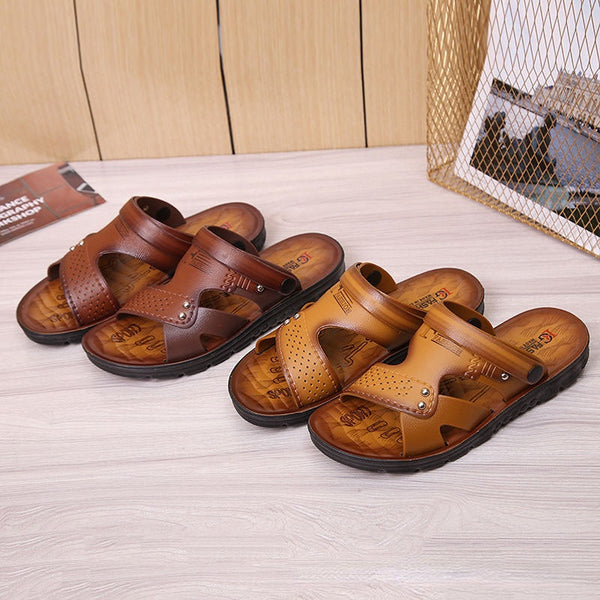 Twee paar leren herensandalen in bruin en camel op houten vloer, met open teen en geperforeerd ontwerp. Comfortabele zomerschoenen voor heren.