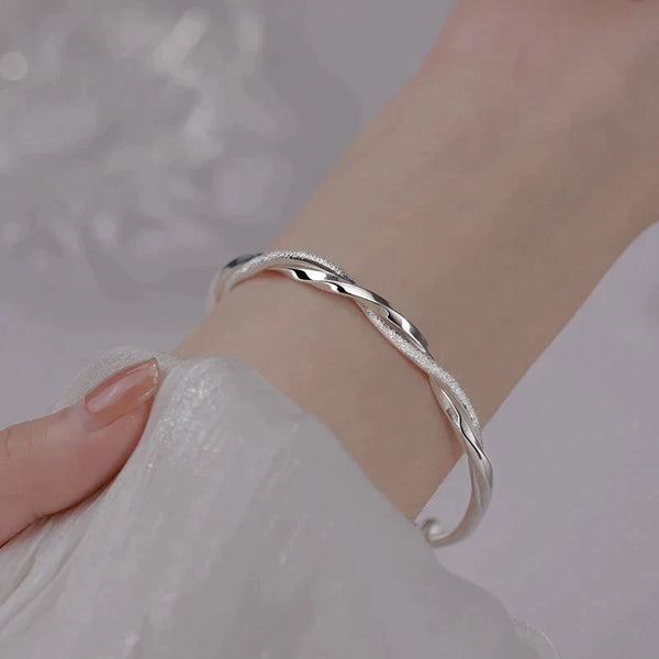 Zilveren gedraaide armband op pols, elegant en minimalistisch ontwerp, perfect voor modieuze sieradenliefhebbers. Geschikt voor dagelijks gebruik.