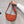 Oranje schoudertas van stof, vastgehouden door een hand tegen een grijze muur. Modieuze crossbody tas, ideaal voor dagelijks gebruik.