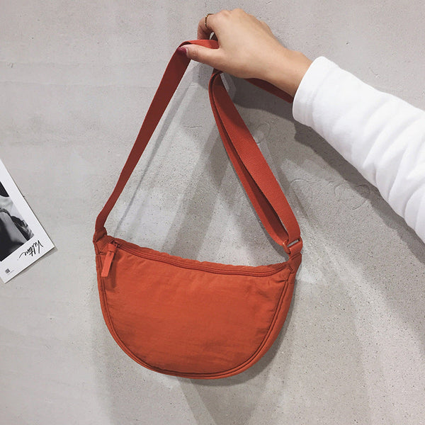 Oranje schoudertas van stof, vastgehouden door een hand tegen een grijze muur. Modieuze crossbody tas, ideaal voor dagelijks gebruik.