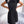 Vrouw in zwarte geplooide jurk met strik, staand voor witte bank. Elegante damesmode, zomerjurk, casual chic outfit, trendy kledingstijl.