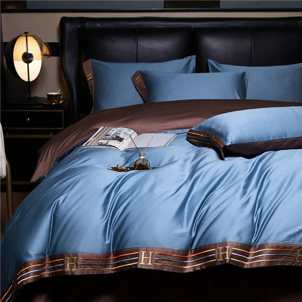 Luxe blauw en bruin dekbedovertrek met H-patroon, satijnen afwerking, opgemaakt bed, moderne slaapkamer, stijlvolle interieurdecoratie.
