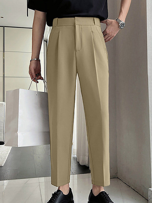 Man in zwarte top en beige pantalon met plooien, houdt witte papieren tas vast. Stijlvolle herenkleding, moderne mode, casual outfit.
