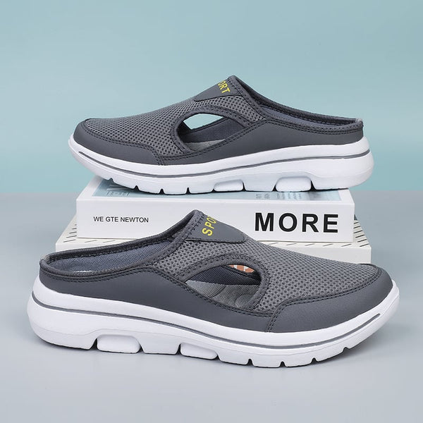 Grijze sportieve instapschoenen met ademend mesh bovenwerk en witte zool, geplaatst op boeken. Comfortabele herenschoenen voor dagelijks gebruik.