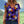 Vrouw draagt kleurrijk bloemen T-shirt met viooltjesprint, tegen een zonnige, groene achtergrond. Perfect voor zomermode en casual outfits.