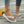 Witte teenslippers met vlinderdecoratie, gedragen door vrouw op houten vloer, naast zonnebloem. Perfect voor zomerse casual outfits.