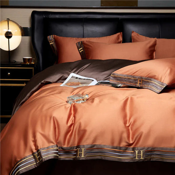 Luxe oranje en bruine satijnen dekbedovertrekset met initialen "H", inclusief kussenslopen en bedlamp, perfect voor moderne slaapkamerinrichting.