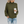 Vrouw in groene gebreide trui met col, houdt een kartonnen koffiebeker vast, draagt gescheurde blauwe jeans. Casual herfstmode, comfortabele stijl.