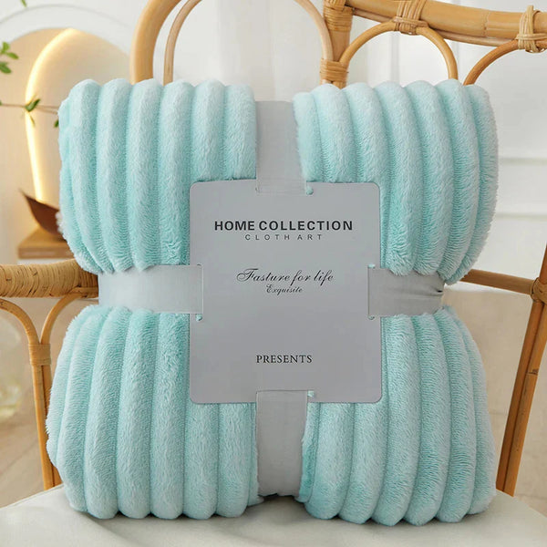 Zachte turquoise fleece deken, Home Collection, verpakt met grijze band, op rotan stoel. Perfect voor interieurdecoratie en comfort.