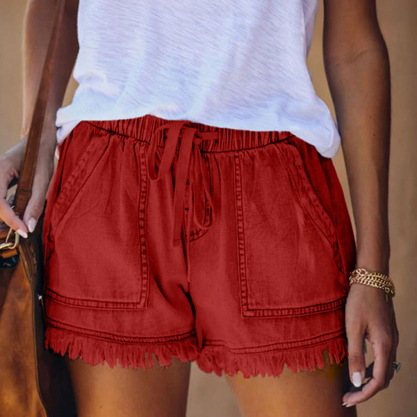 Vrouw draagt rode katoenen shorts met franjes en elastische tailleband, gecombineerd met een witte top. Perfecte zomermode voor casual outfits.
