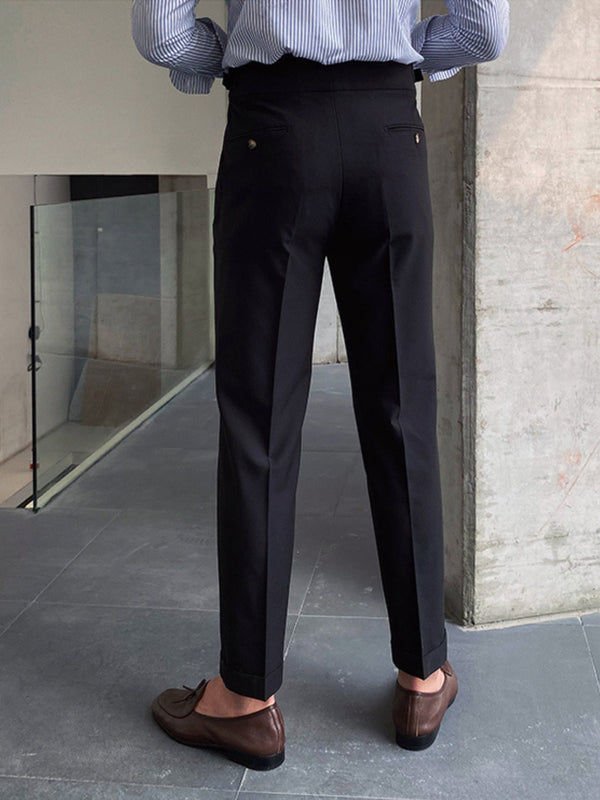 Man in zwarte broek en bruine loafers, staand op grijze tegelvloer. Stijlvolle herenkleding, zakelijke outfit, moderne mode.