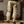 Man in beige cargobroek en bruine laarzen, houdt een grote tas vast in een rustieke kamer. Casual herenkleding, outdoor mode, comfortabele stijl.