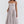 Vrouw in elegante, lichtgrijze midi-jurk met spaghettibandjes en geplooide rok. Perfect voor zomerfeesten en bruiloften. Modieuze dameskleding.