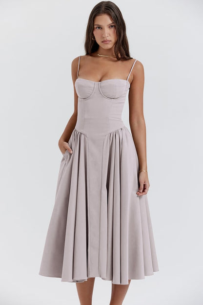Vrouw in elegante, lichtgrijze midi-jurk met spaghettibandjes en geplooide rok. Perfect voor zomerfeesten en bruiloften. Modieuze dameskleding.