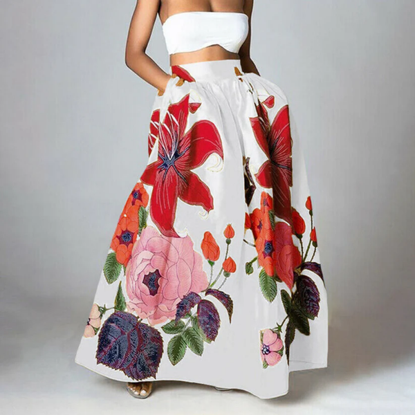 Vrouw in witte strapless top en lange rok met kleurrijke bloemenprint, waaronder rode lelies en roze rozen, op grijze achtergrond.