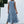 Vrouw in lichtblauwe maxi-jurk met ruches, staand voor witte muur. Zomermode, casual stijl, elegante dameskleding, boho-chic look.