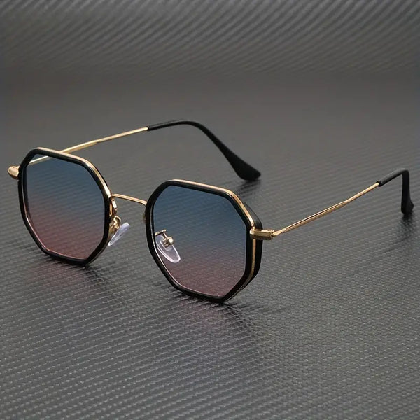 Zeshoekige zonnebril met gouden montuur en blauw getinte glazen op een grijze achtergrond. Stijlvolle unisex zonnebril, modieuze accessoires.