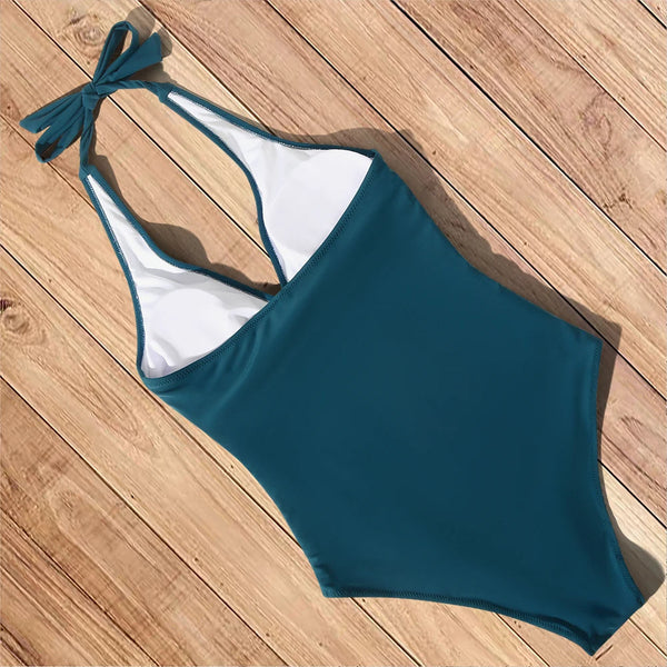 Groene badpak met halternek en witte voering, liggend op houten vloer. Stijlvol damesbadpak, perfect voor strand en zwembad.