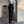 Man in stijlvolle zakelijke outfit met gestreept overhemd, zwarte pantalon en bruine loafers, leunend tegen een betonnen muur in moderne kantooromgeving.