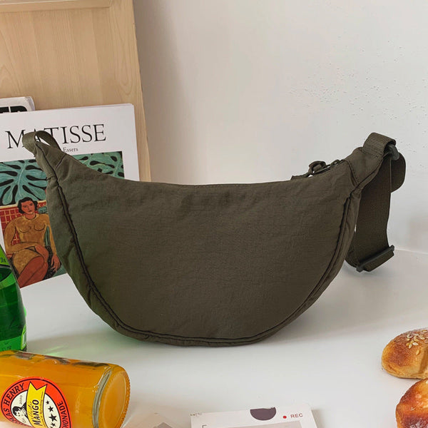 Olijfgroene crossbody tas op tafel naast Matisse-poster, fles en broodjes. Stijlvolle schoudertas voor dagelijks gebruik, modieus en praktisch.